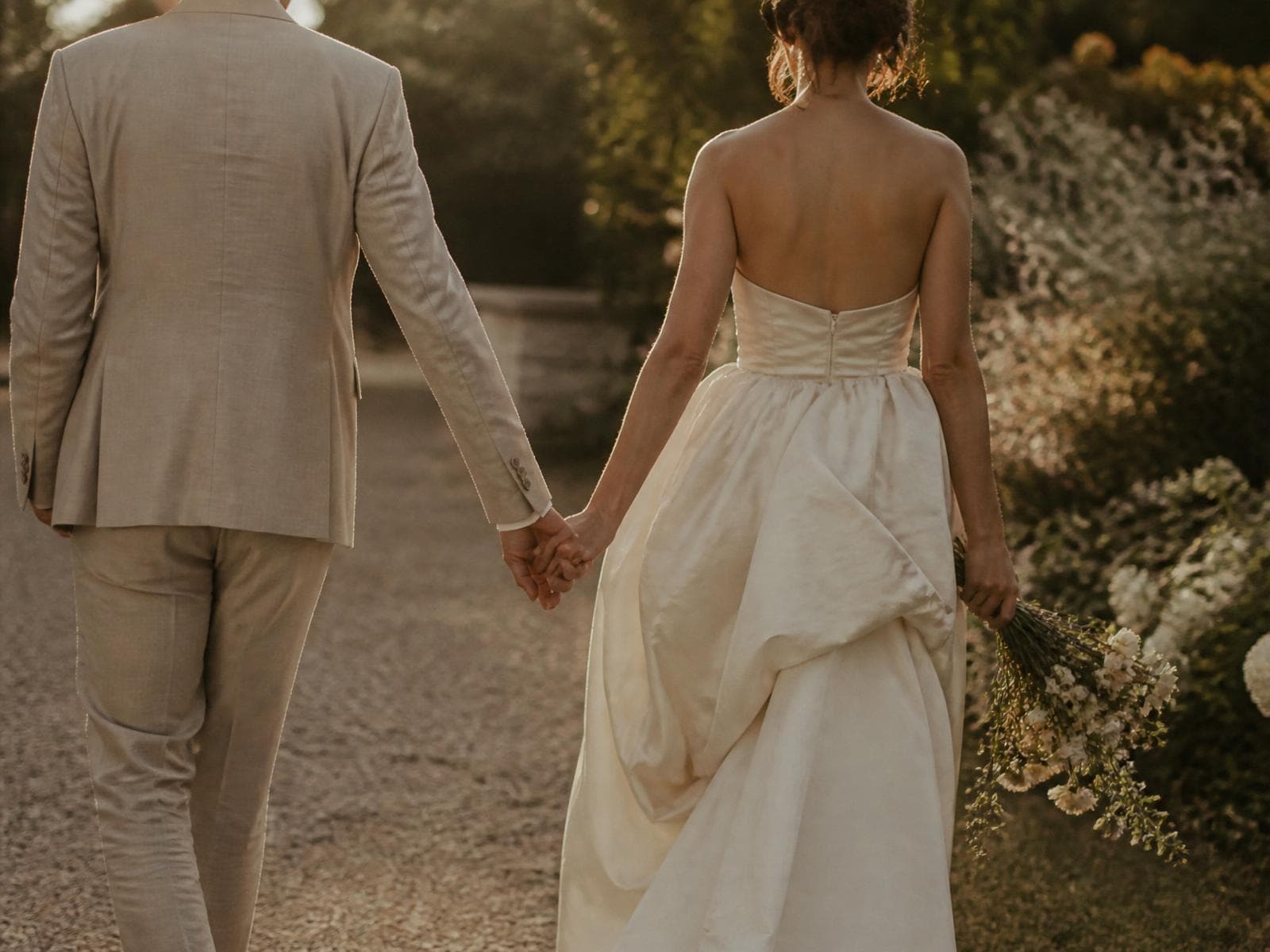 A couple walking hand in hand through a sunlit garden